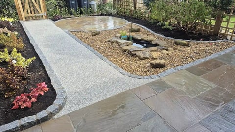 Backyard landscaping with gravel beds, concrete pathways, paved patio, and surrounding garden plants