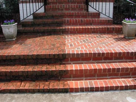 Red brick entry staircase with metal railings and potted flowers on either side
