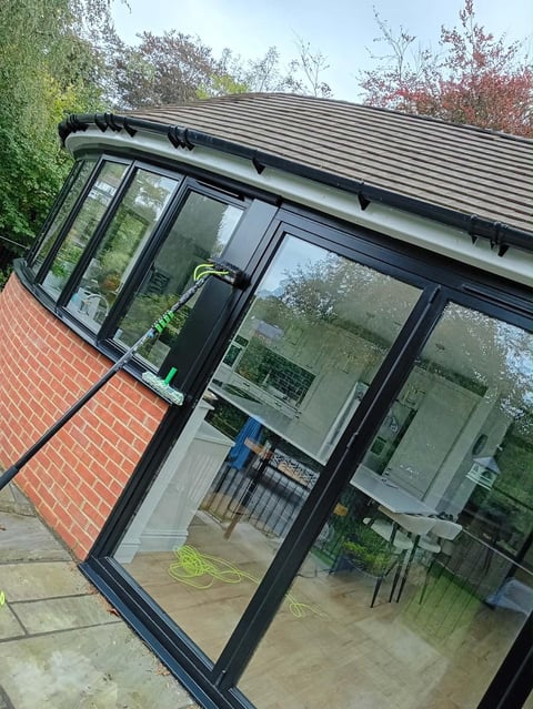 Modern black glass and metal conservatory extension attached to brick house with corrugated roof