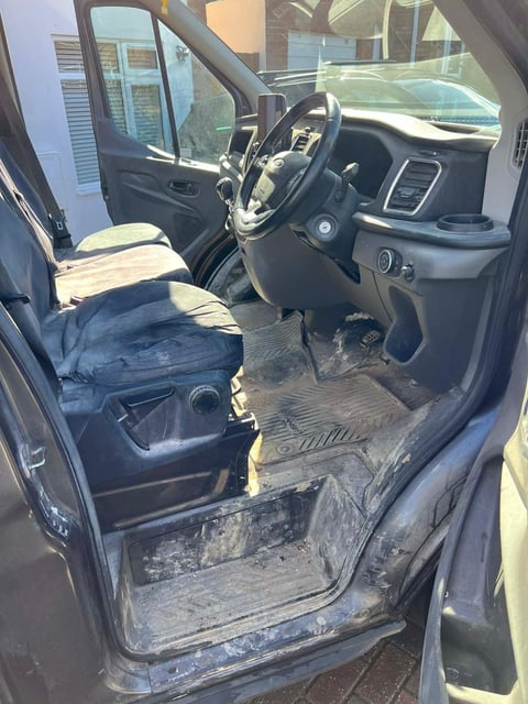 Interior view of a truck cab with steering wheel, dashboard, and muddy floor, door open to the side
