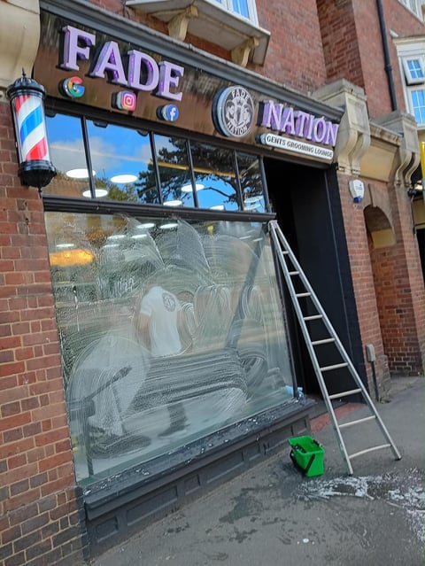Barber shop storefront with Fade Nation signage, large window with soaped glass, red brick building, and a ladder outside